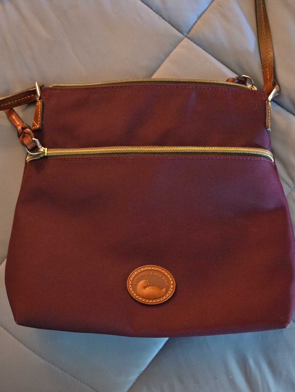Dooney & Bourke burgundy nylon crossbody bag featuring a front zip pocket,